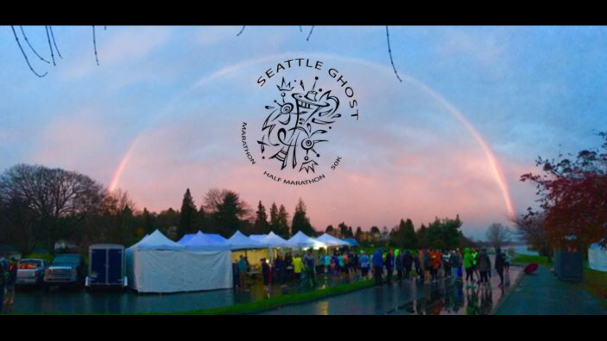 The Seattle Ghost logo over a rainbow at the finish area, with the aid tents and runners below